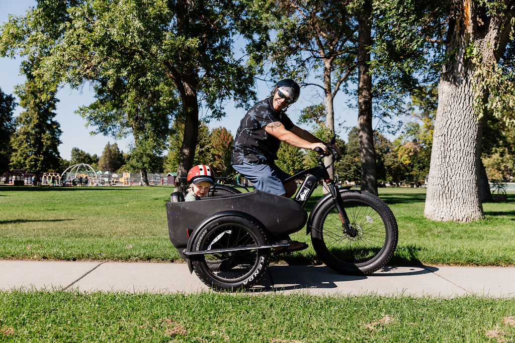 Photo of Big-E Bikes founder, Kelly Bigelow riding the thunderbolt with sidecar and his son in it.